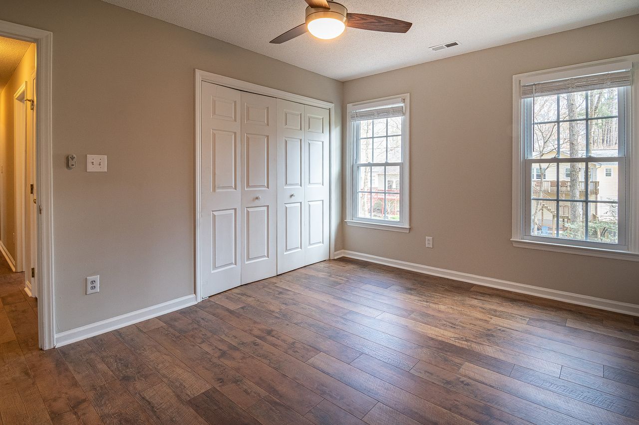 portfolio-08 Spacious empty room with hardwood floors, ceiling fan, and natural light from windows.