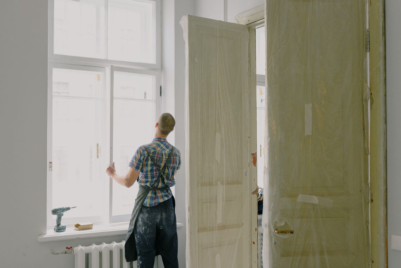 portfolio-04 Back view of unrecognizable workman in apron mounting window near drilling machine and doors in flat