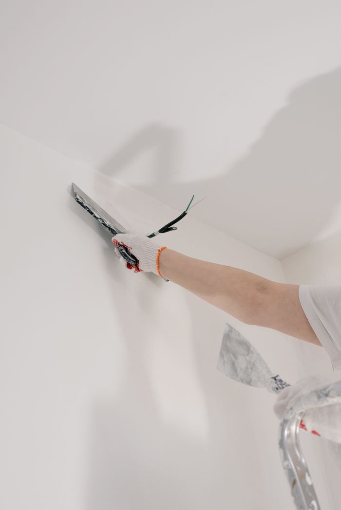 gallery-04 Crop unrecognizable male in gloves holding tool while standing on ladder and renovating walls in flat
