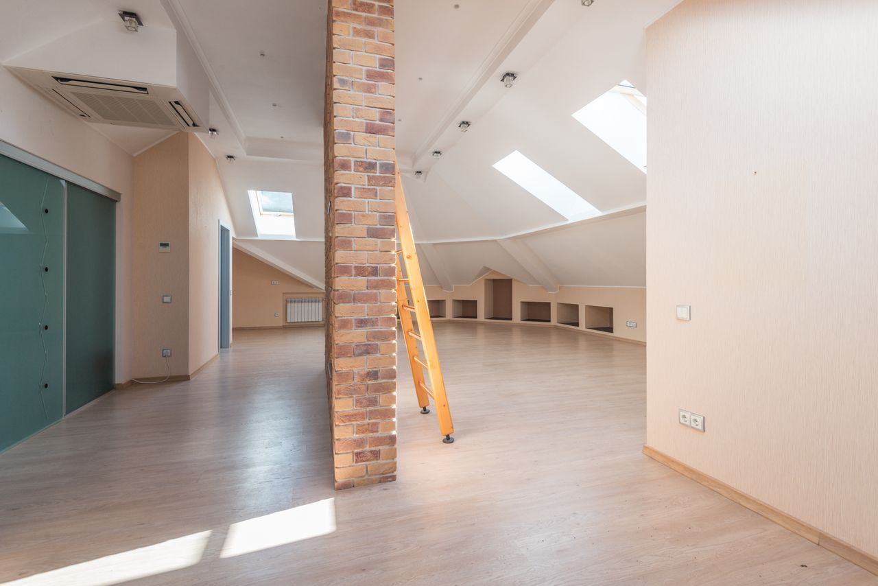 cta-02 Spacious attic room with natural light from skylights, featuring a brick pillar and a wooden ladder.